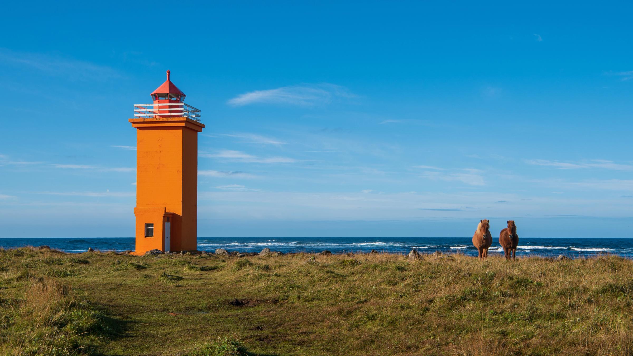 un faro de color naranja junto a dos caballos islandeses