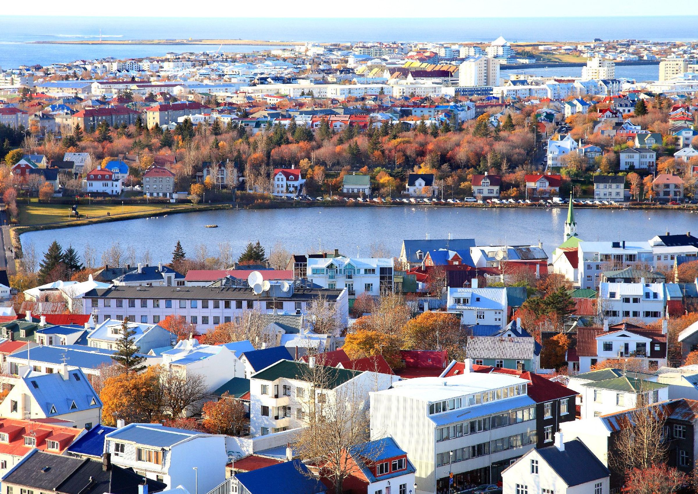 Aerial view of a city with colorful houses, autumn trees, and a lake.