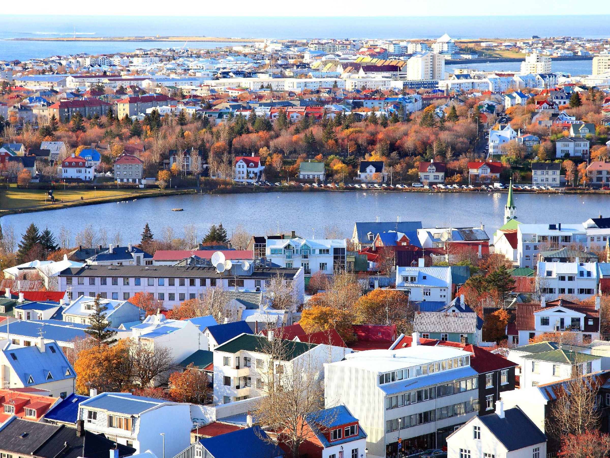 Aerial view of a city with colorful houses, autumn trees, and a lake.