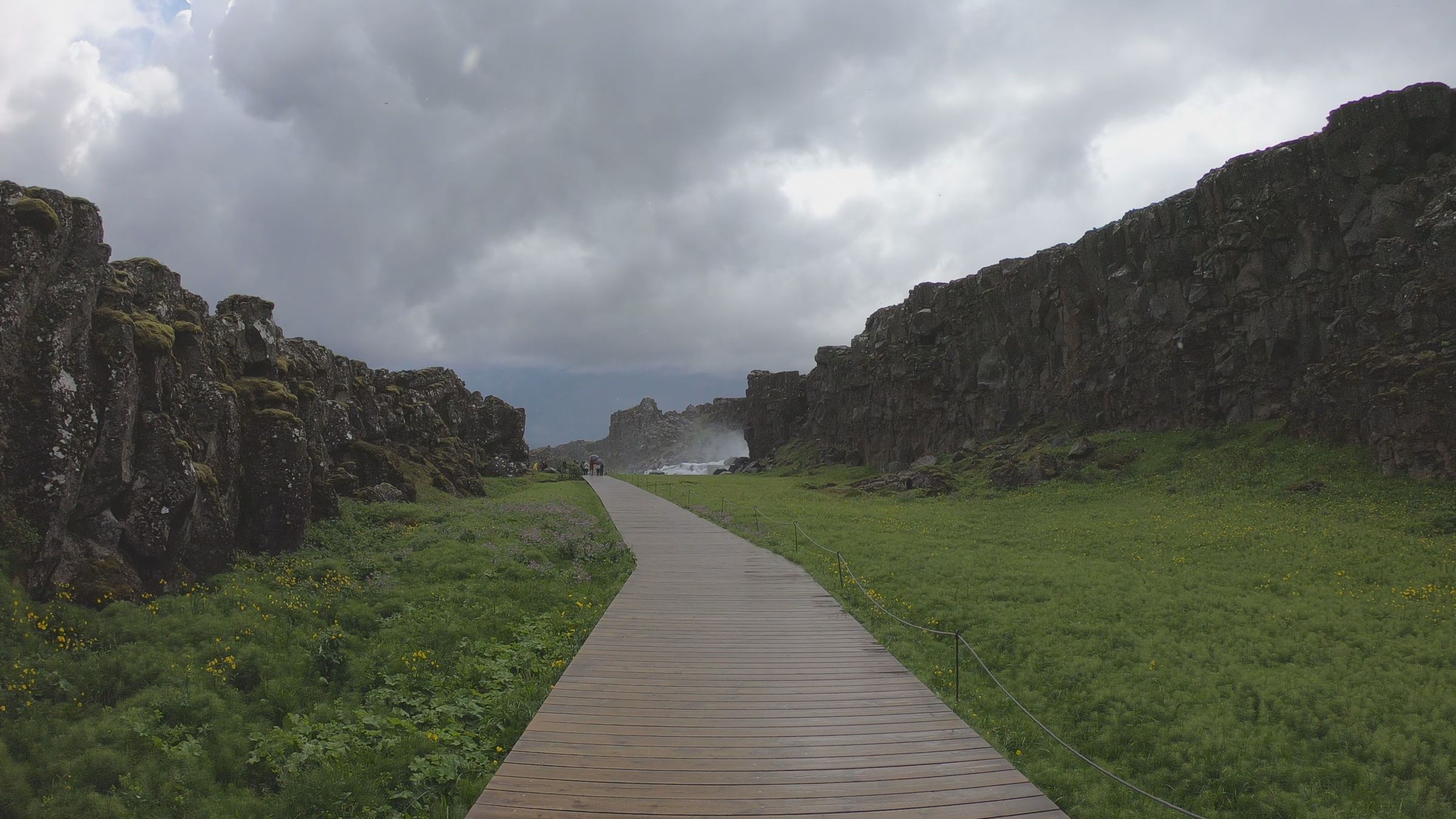 a wooden walkway going through a grassy field with a mountain in the background .
