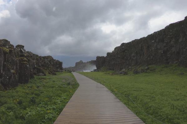 a wooden walkway going through a grassy field with a mountain in the background .