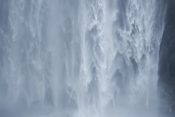woman in yellow jacket standing at the base of a powerful waterfall