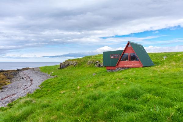 a small red and green house is sitting on top of a grassy hill next to the ocean .