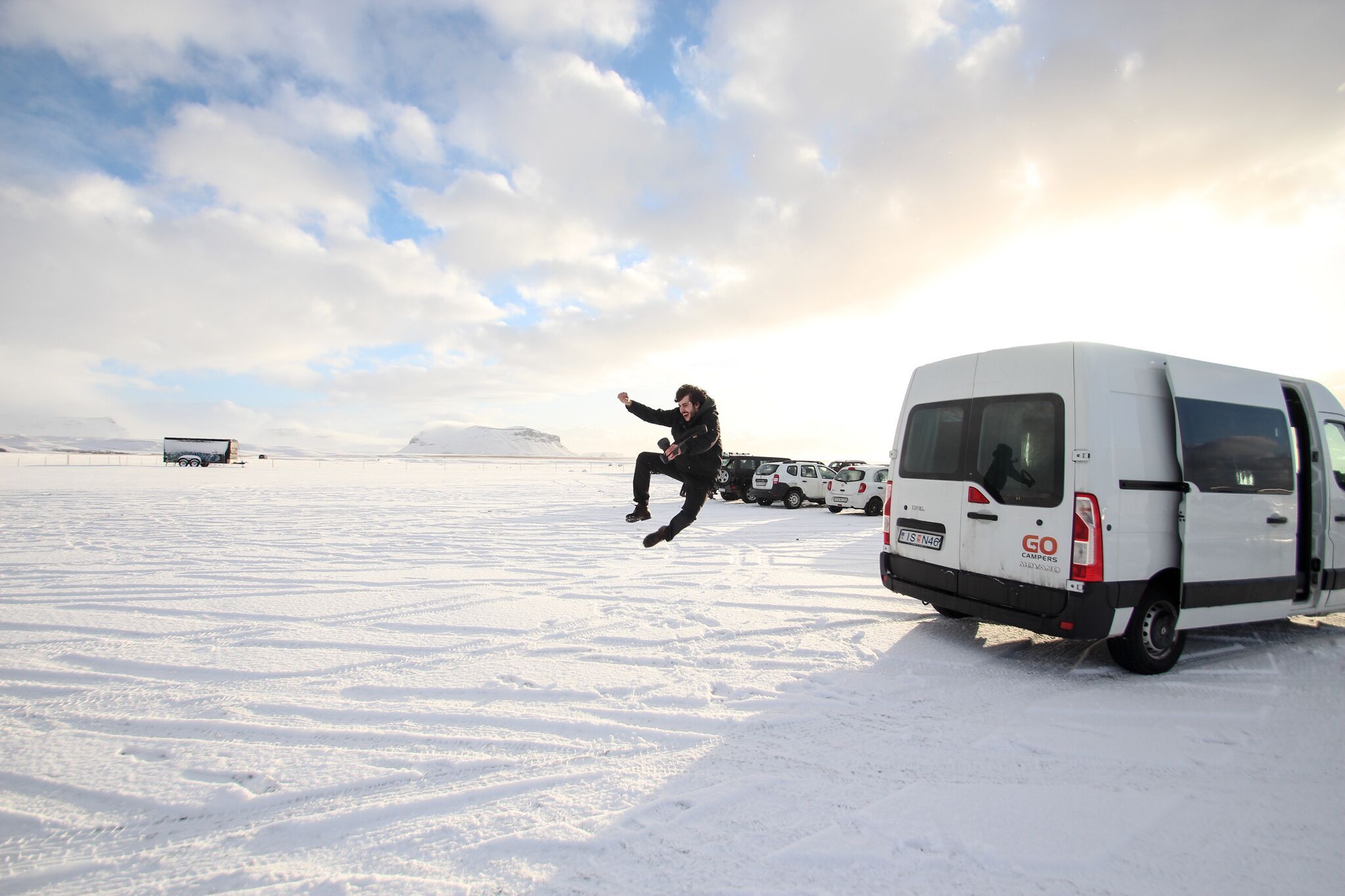 a man is jumping in the air in front of a van in the snow .