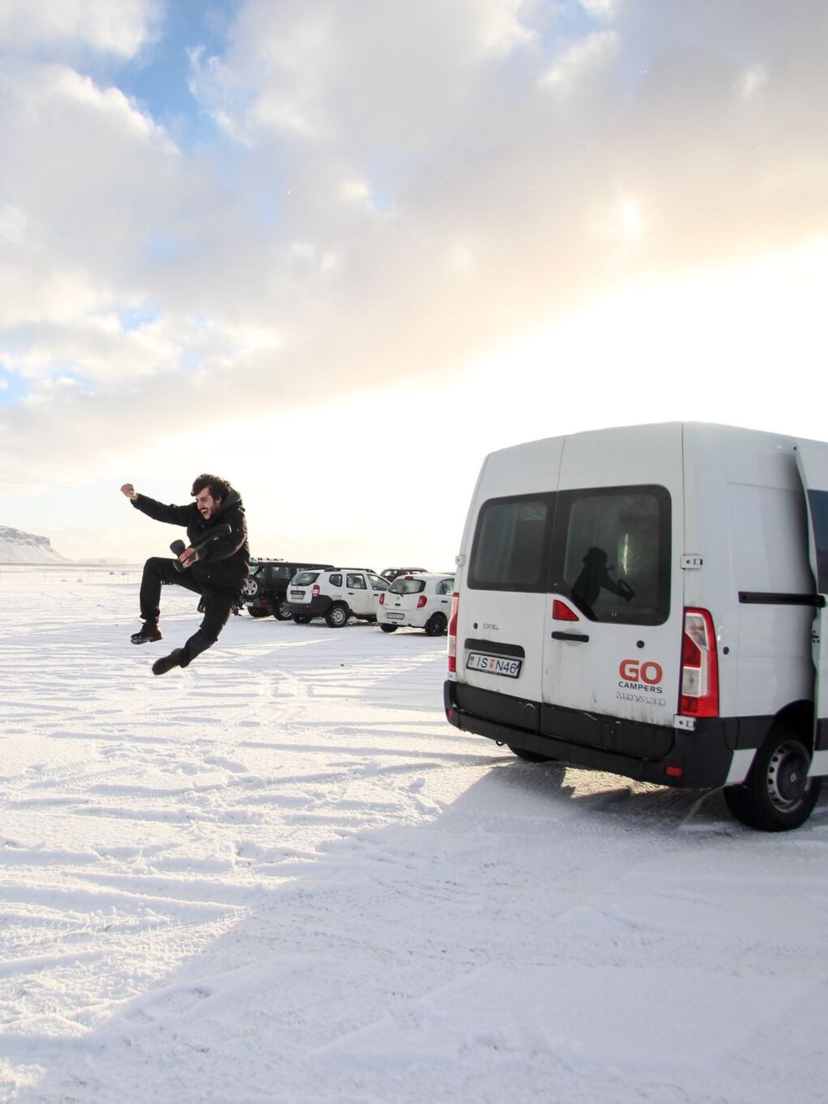 a man is jumping in the air in front of a van in the snow .