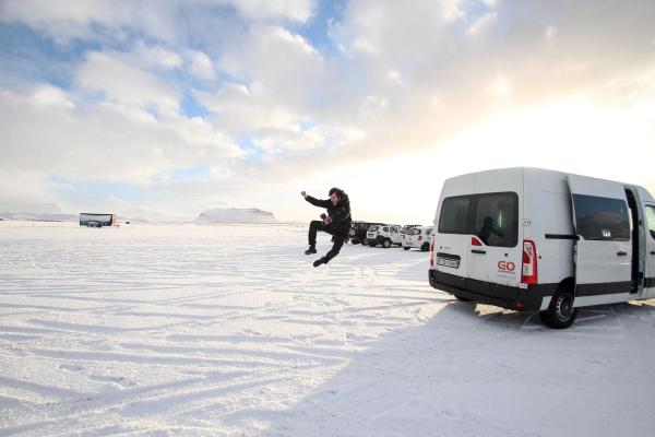 A person jumps in a snowy landscape beside a white rental van with open doors.