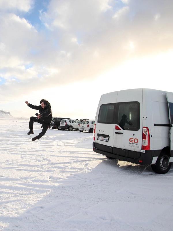 a man is jumping in the air in front of a van in the snow .