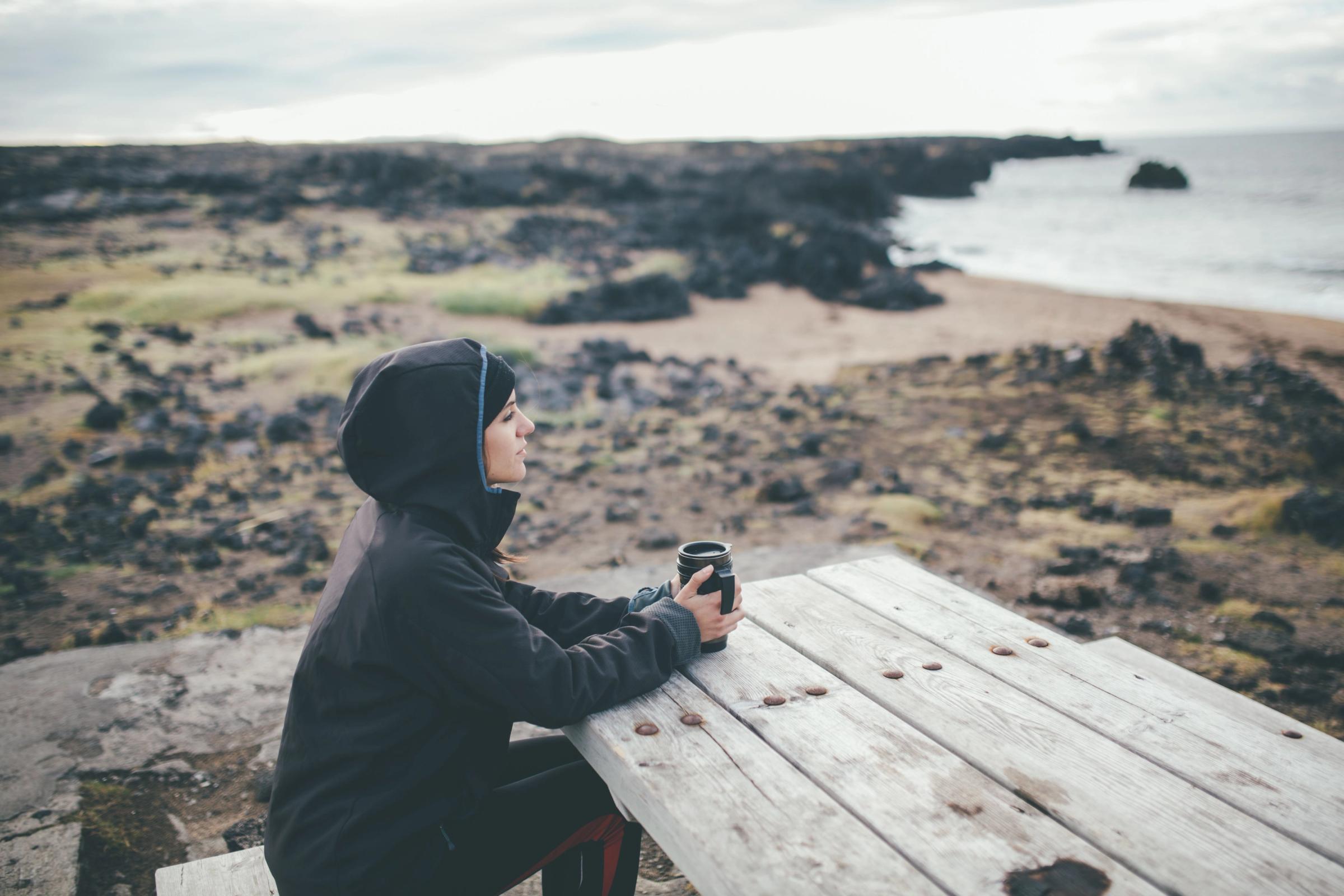 Girl with waterproof jacket drinking a coffee in a bench, Iceland
