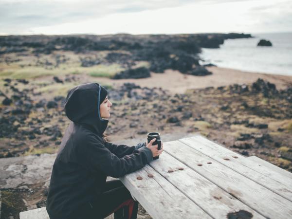 Girl with waterproof jacket drinking a coffee in a bench, Iceland