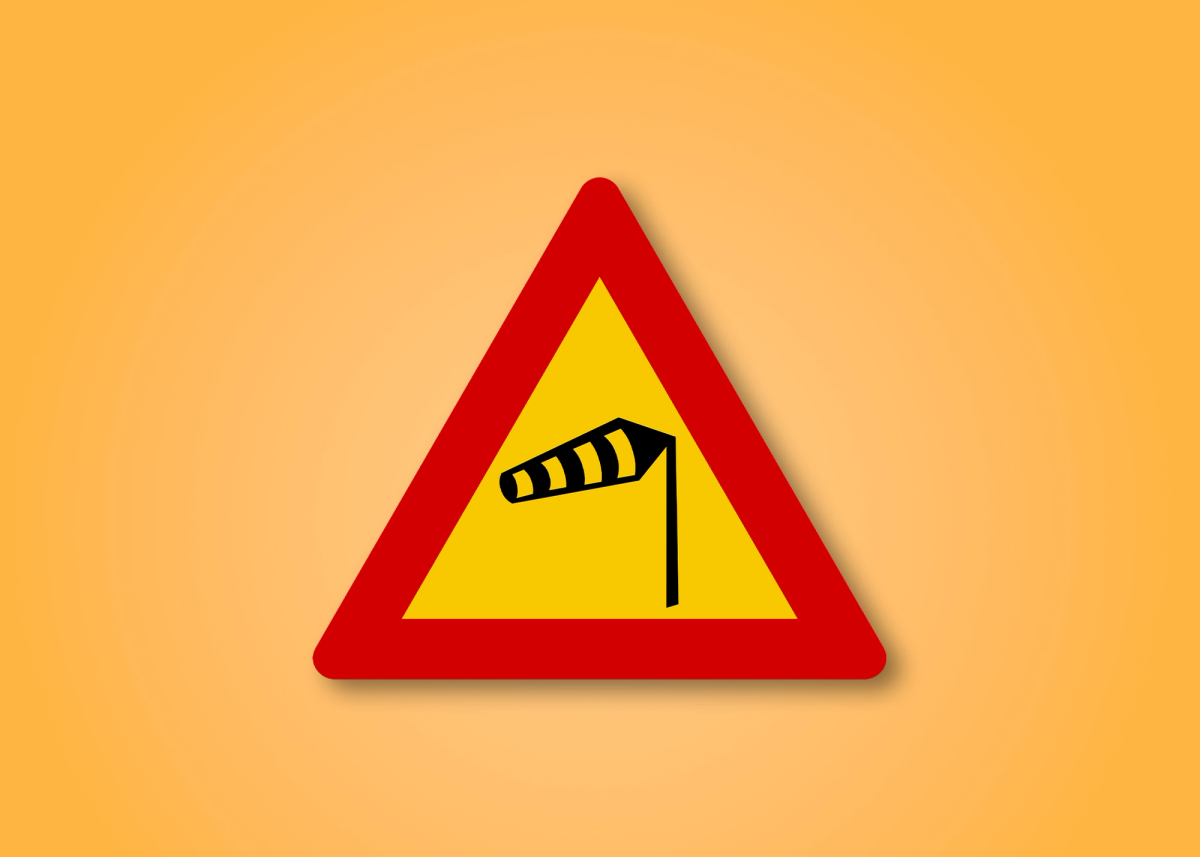 Red and yellow triangle road sign with a wind in the middle. This road sign means Crosswinds