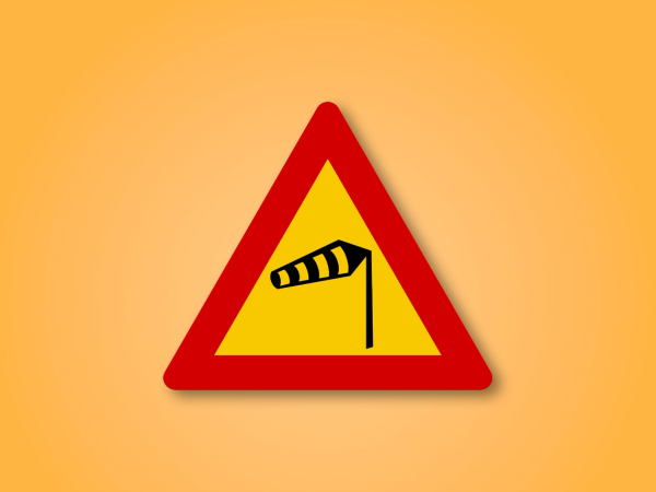 Red and yellow triangle road sign with a wind in the middle. This road sign means Crosswinds