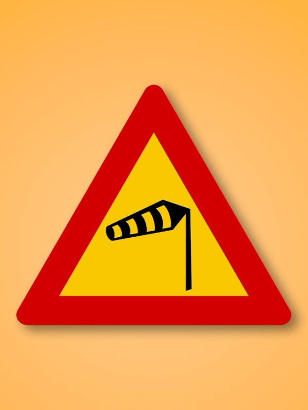Red and yellow triangle road sign with a wind in the middle. This road sign means Crosswinds