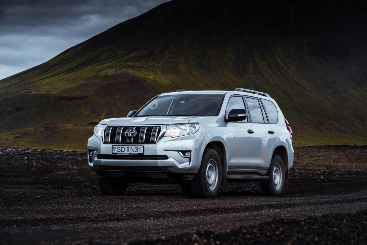 Toyota Land Cruiser self drive Iceland parked on black gravel below a mossy hillside