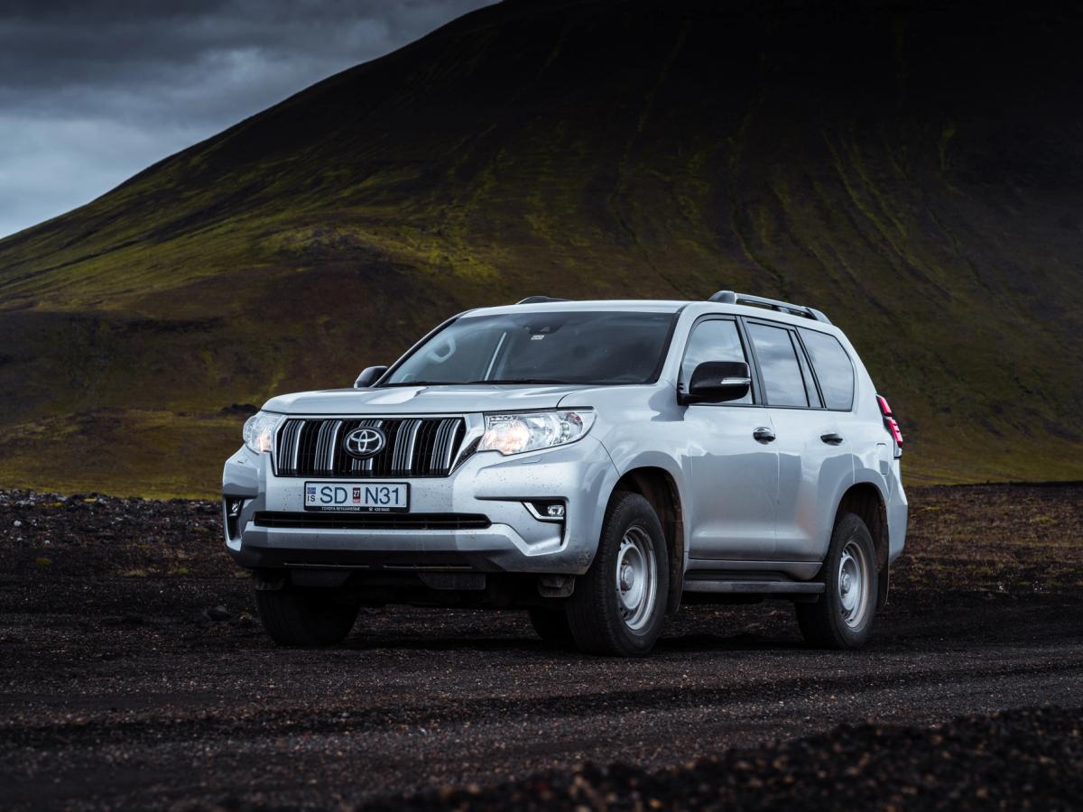 Land Cruiser – Frontansicht Toyota Land Cruiser für eine Selbstfahrerreise durch Island, geparkt auf schwarzem Schotter unterhalb eines moosbewachsenen Hangs