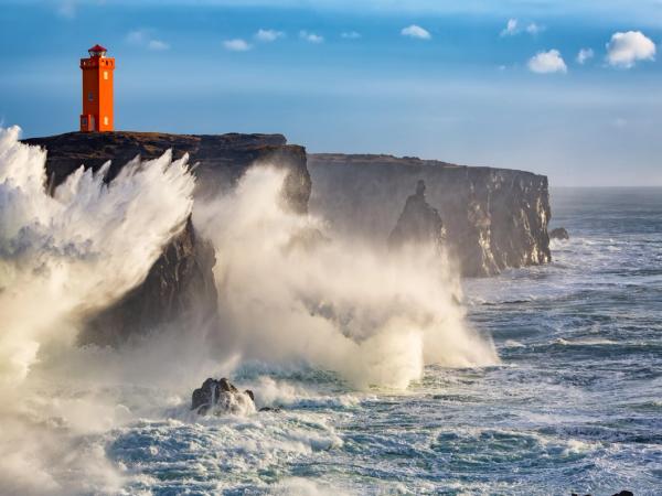 a lighthouse on a cliff overlooking the ocean with waves crashing against it .