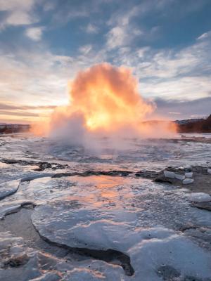 un géiser está entrando en erupción en medio de un lago congelado al atardecer.