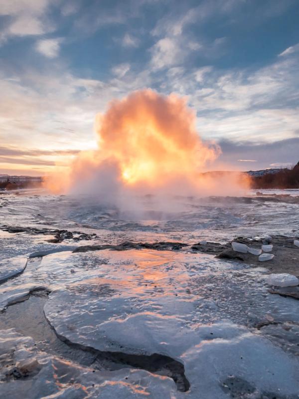 un géiser está entrando en erupción en medio de un lago congelado al atardecer.