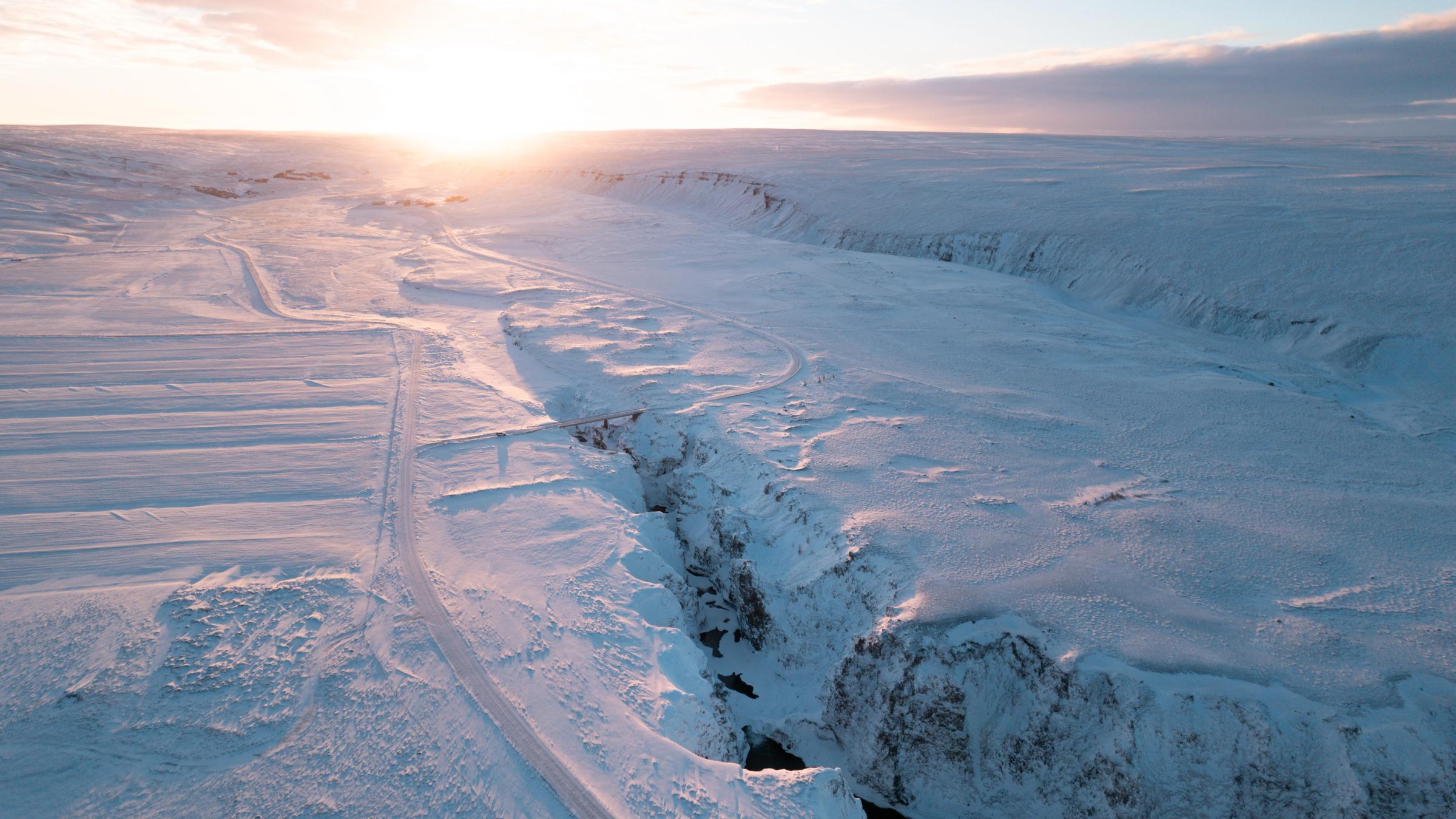 A snow-covered canyon at sunrise with a bright sun on the horizon.