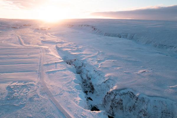A snow-covered canyon at sunrise with a bright sun on the horizon.
