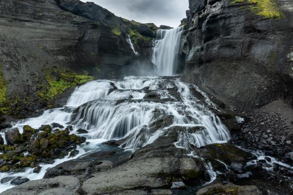 Long exposure of a waterfall cascading over dark, moss-covered rocks.