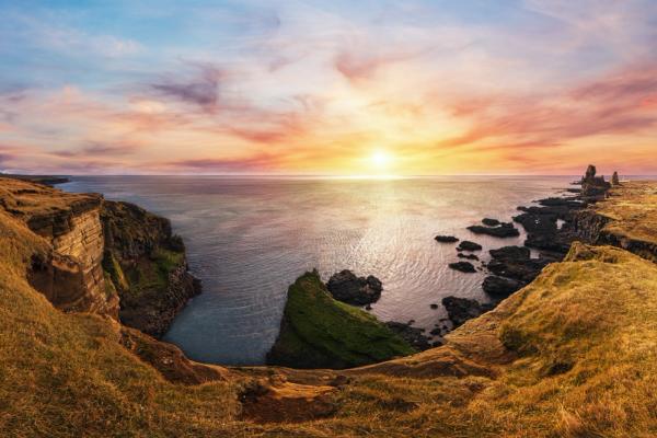 a sunset over a cliff overlooking the ocean with a castle in the distance .