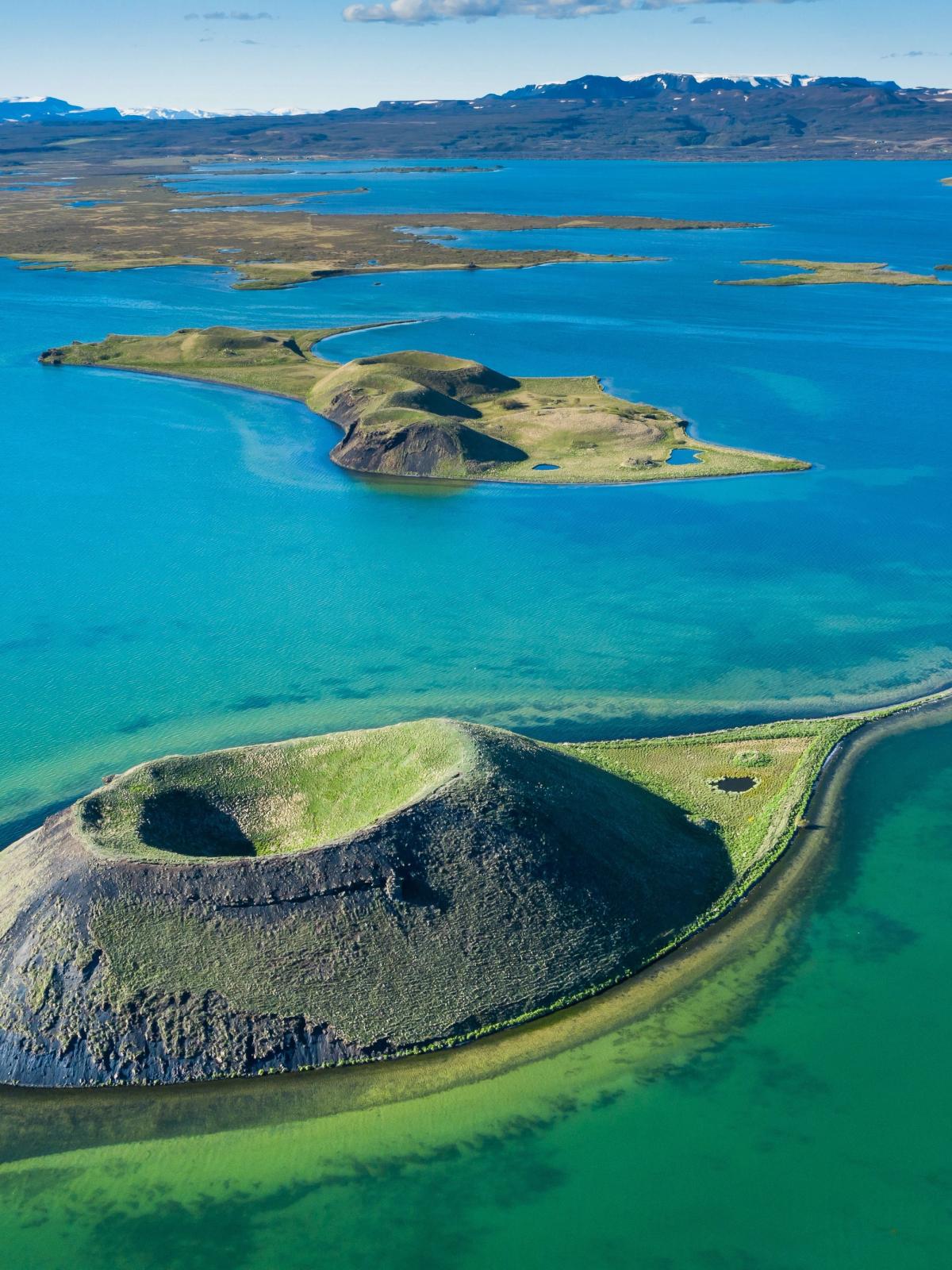 Aerial view of a green volcanic crater island with a land bridge in a turquoise lake.