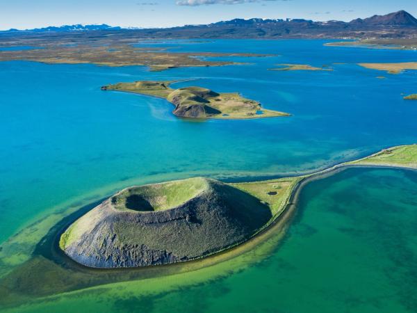 Volcanic crater in a vibrant blue-green lake, with islands and mountains.