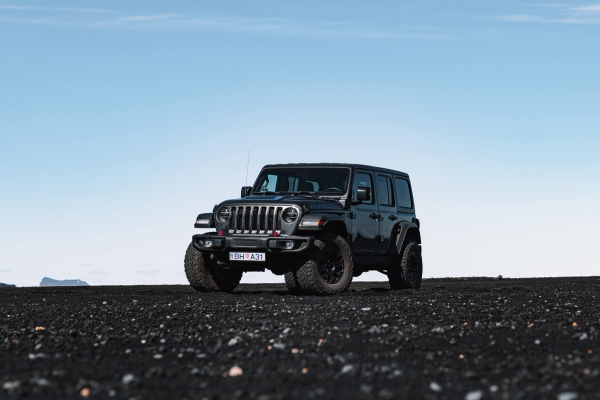 A black Jeep Wrangler parked on a dark, rocky plain under a clear blue sky.