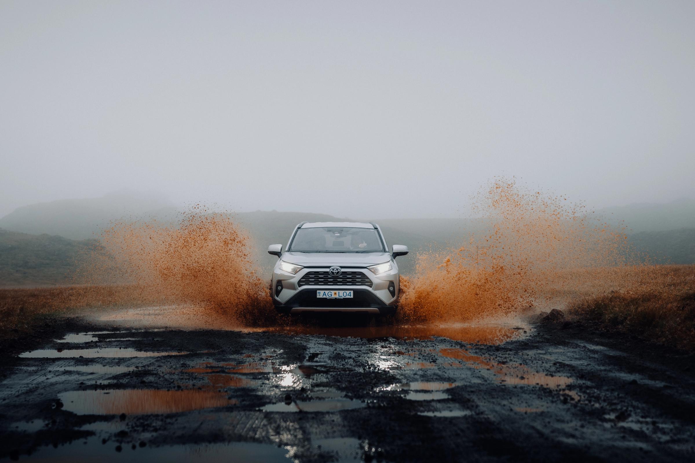 Toyota RAV4 head on through a large puddle on a wet gravel road, mud spraying sideways