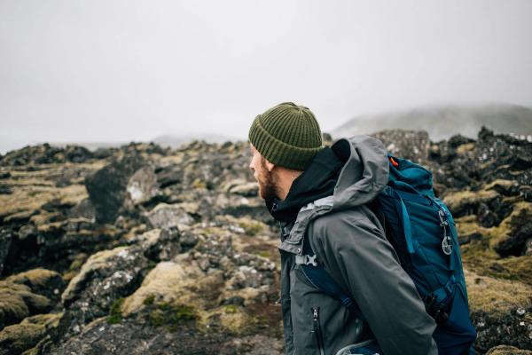 Chico con ropa de senderismo: gorro, chaqueta impermeable, backpack, etc, en un campo lleno de musgo en Islandia