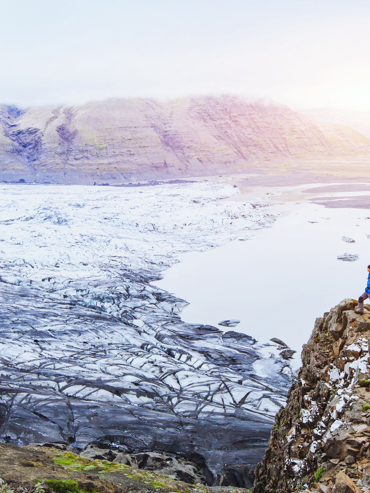 a man is standing on top of a rocky cliff overlooking a glacier .