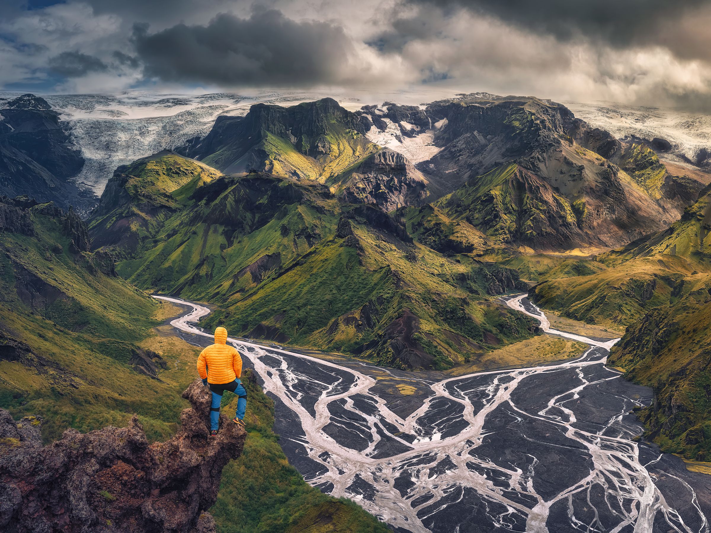 Un homme se tient au sommet d'une montagne surplombant une rivière à Þórsmörk en Islande.