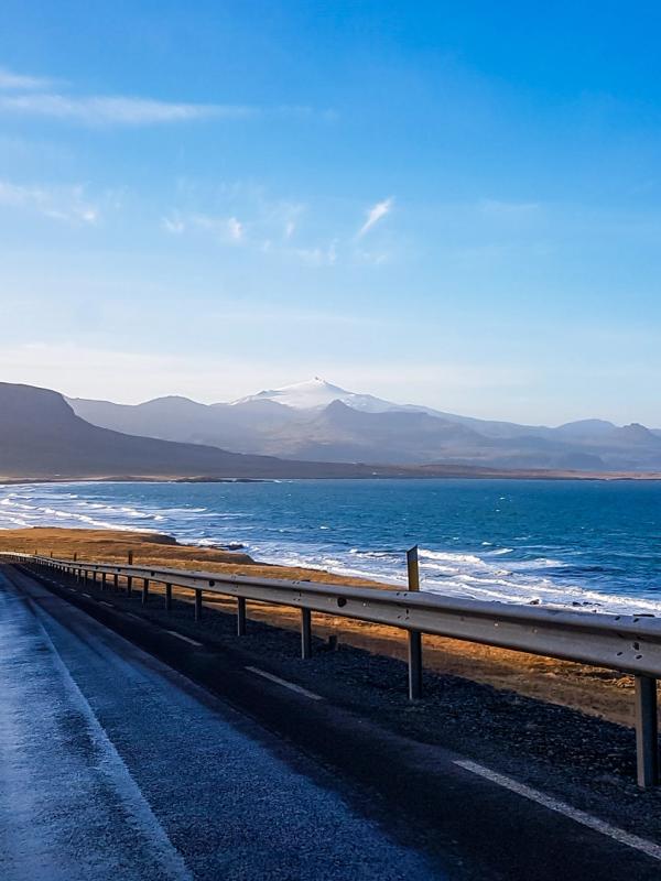 A wet road curves along an ocean coast with distant mountains.
