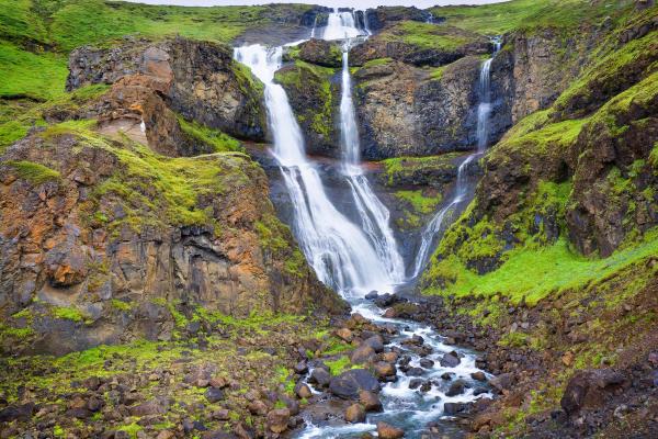 una cascada está rodeada de césped verde y rocas en medio de un valle .