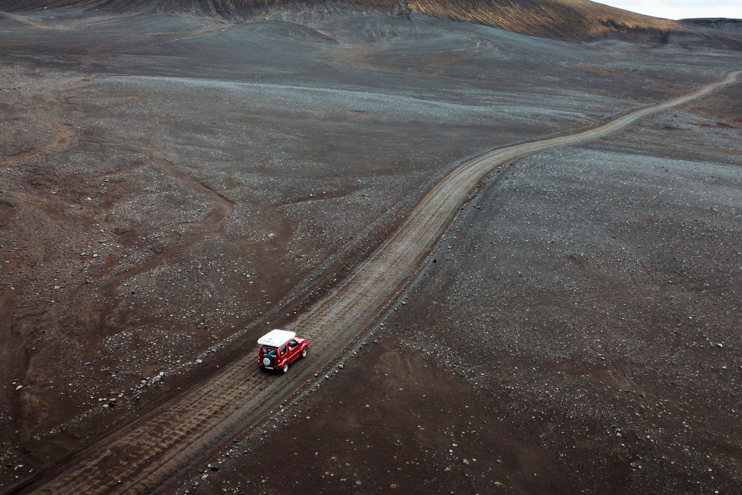 une vue aérienne d'un van rouge roulant sur une route de terre, Hautes Terres d'Islande