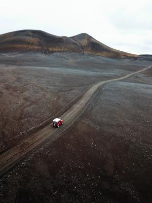 an aerial view of a red van driving down a dirt road .