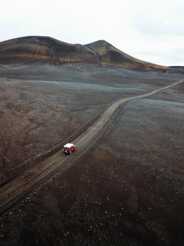an aerial view of a red van driving down a dirt road .