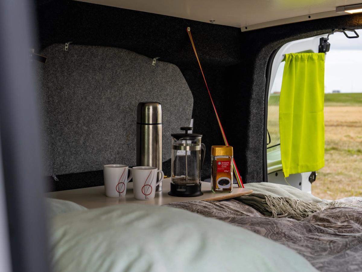 Cafetera y accesorios sobre una mesa Mesa preparada junto a la cama con 2 tazas, un termo y una cafetera de émbolo