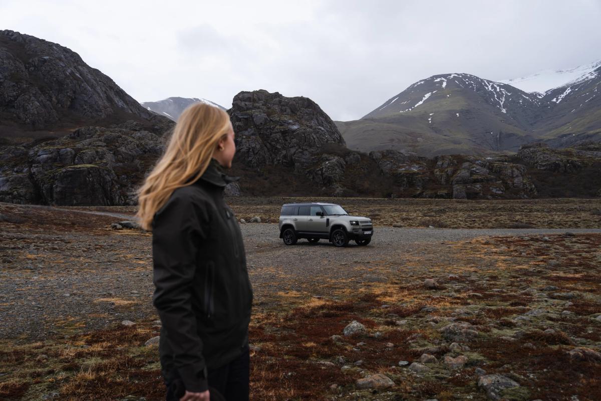 a woman is standing in front of a land rover defender in a field .