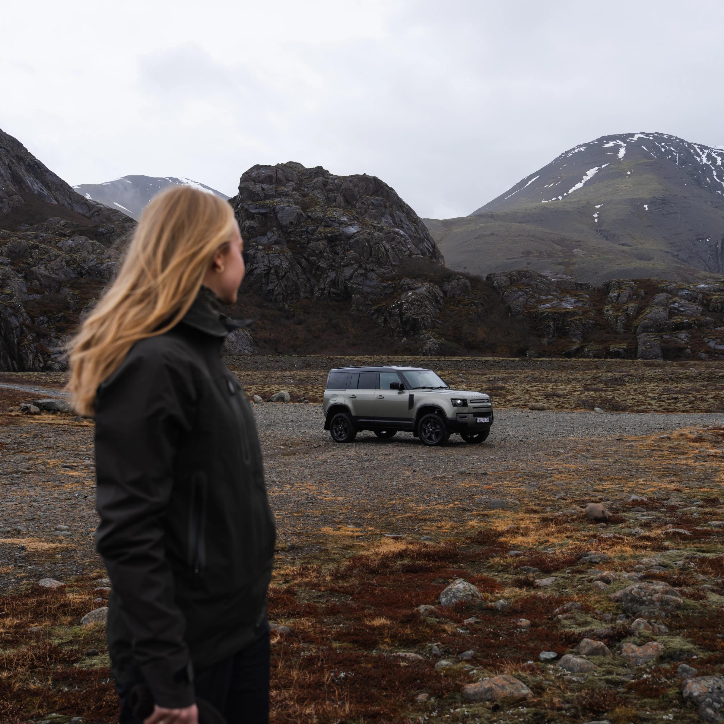 a woman is standing in front of a land rover defender in a field .