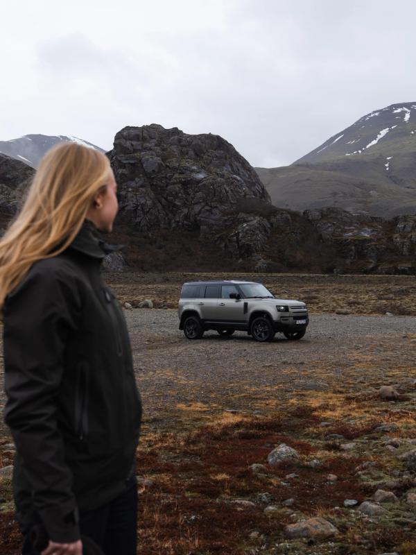 a woman is standing in front of a land rover defender in a field .