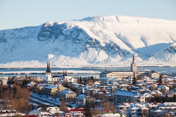 Paisaje urbano nevado con edificios destacados de agujas, un cuerpo de agua y grandes montañas cubiertas de nieve.
