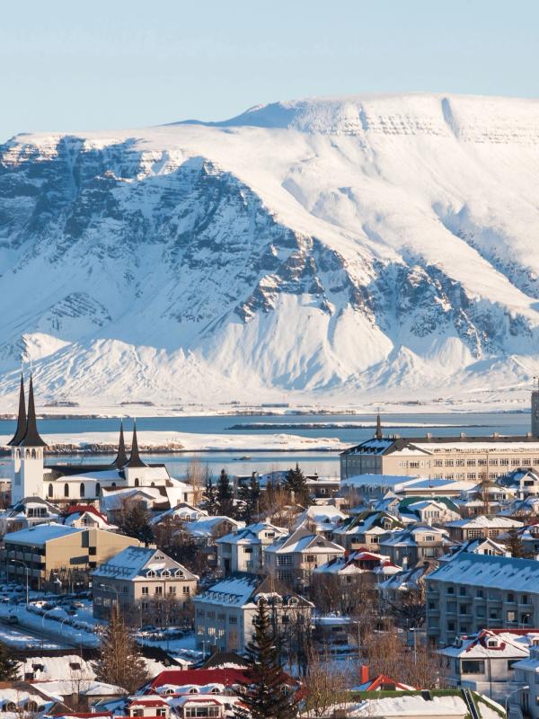 Snowy city with a bay and large snow-covered mountains in the background.