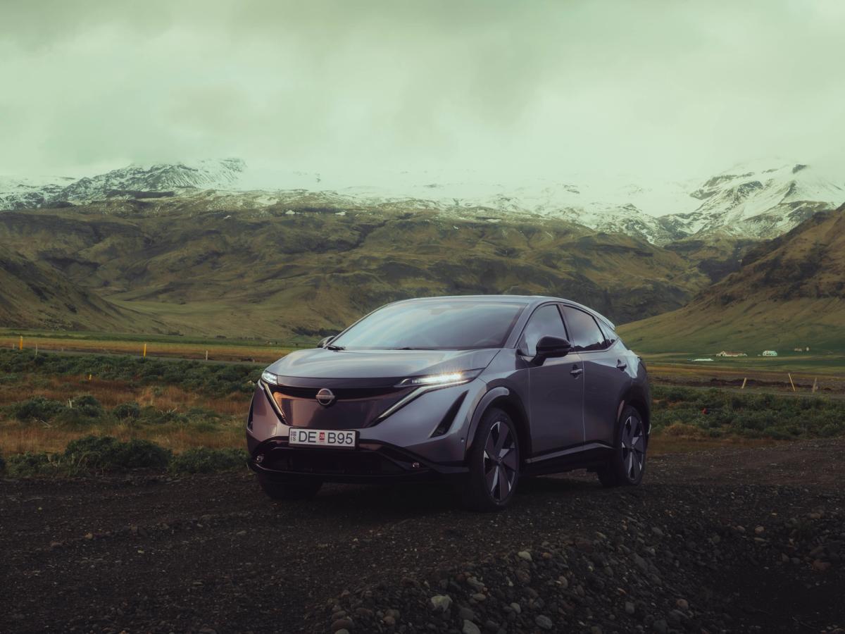 Nissan Ariya með útsýni yfir fjalladal Nissan Ariya lagt á malarvegi með snæviþakin fjöll í bakgrunni