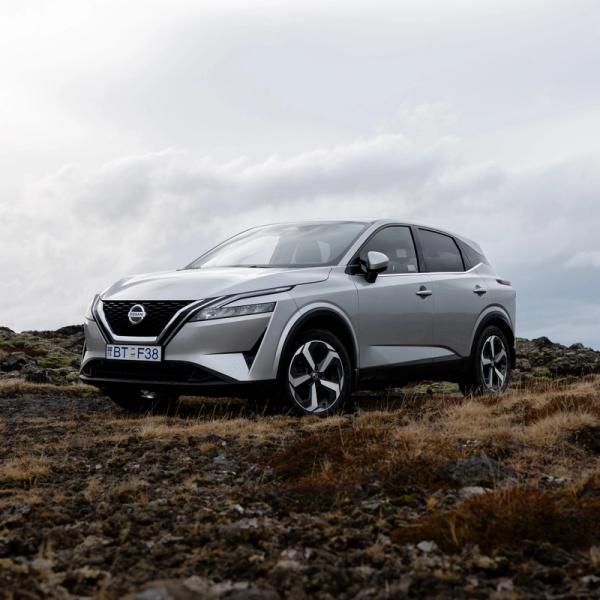 Silver Nissan Qashqai SUV parked on rocky, dry ground under a cloudy sky.