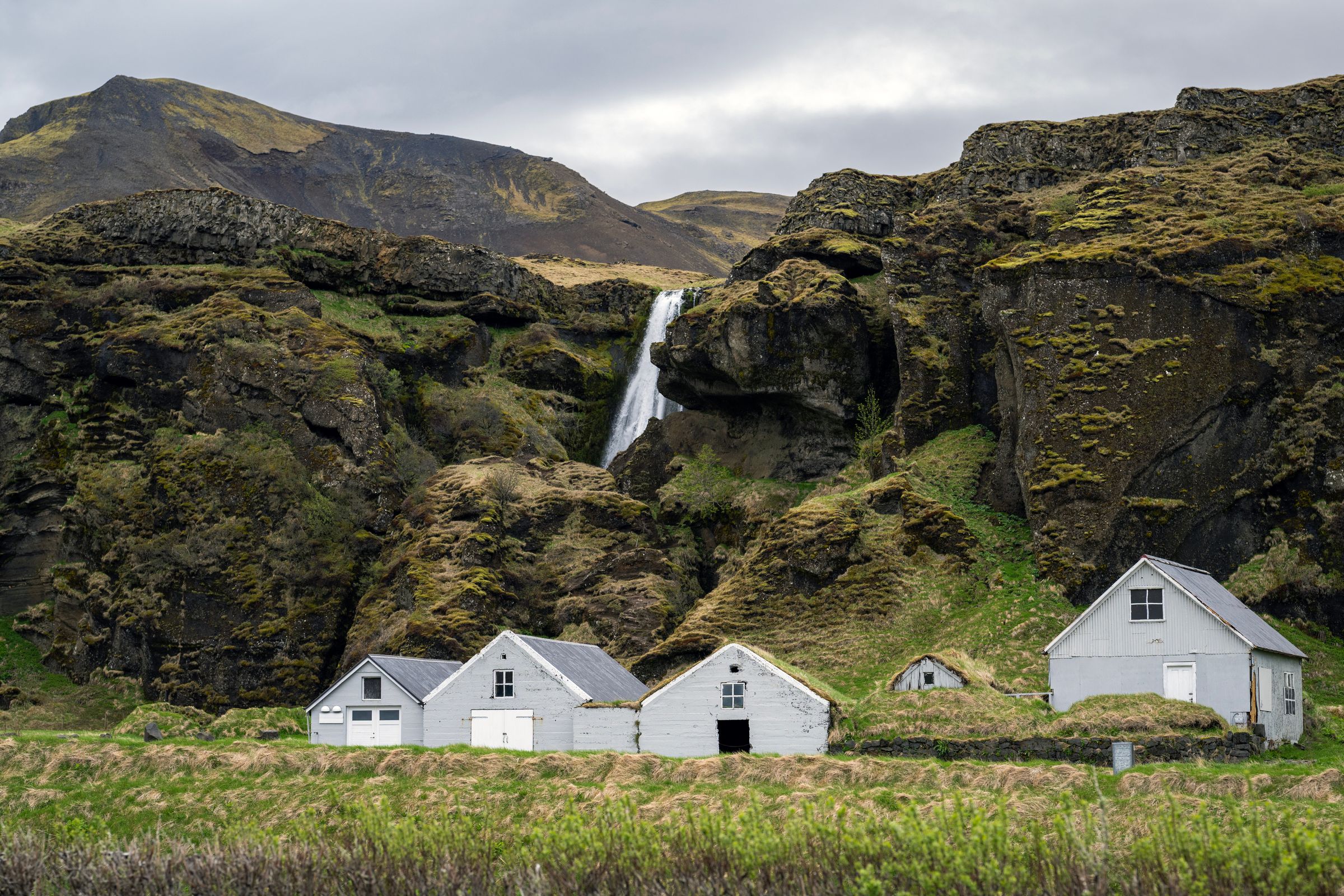 a waterfall is behind a row of houses in the mountains .
