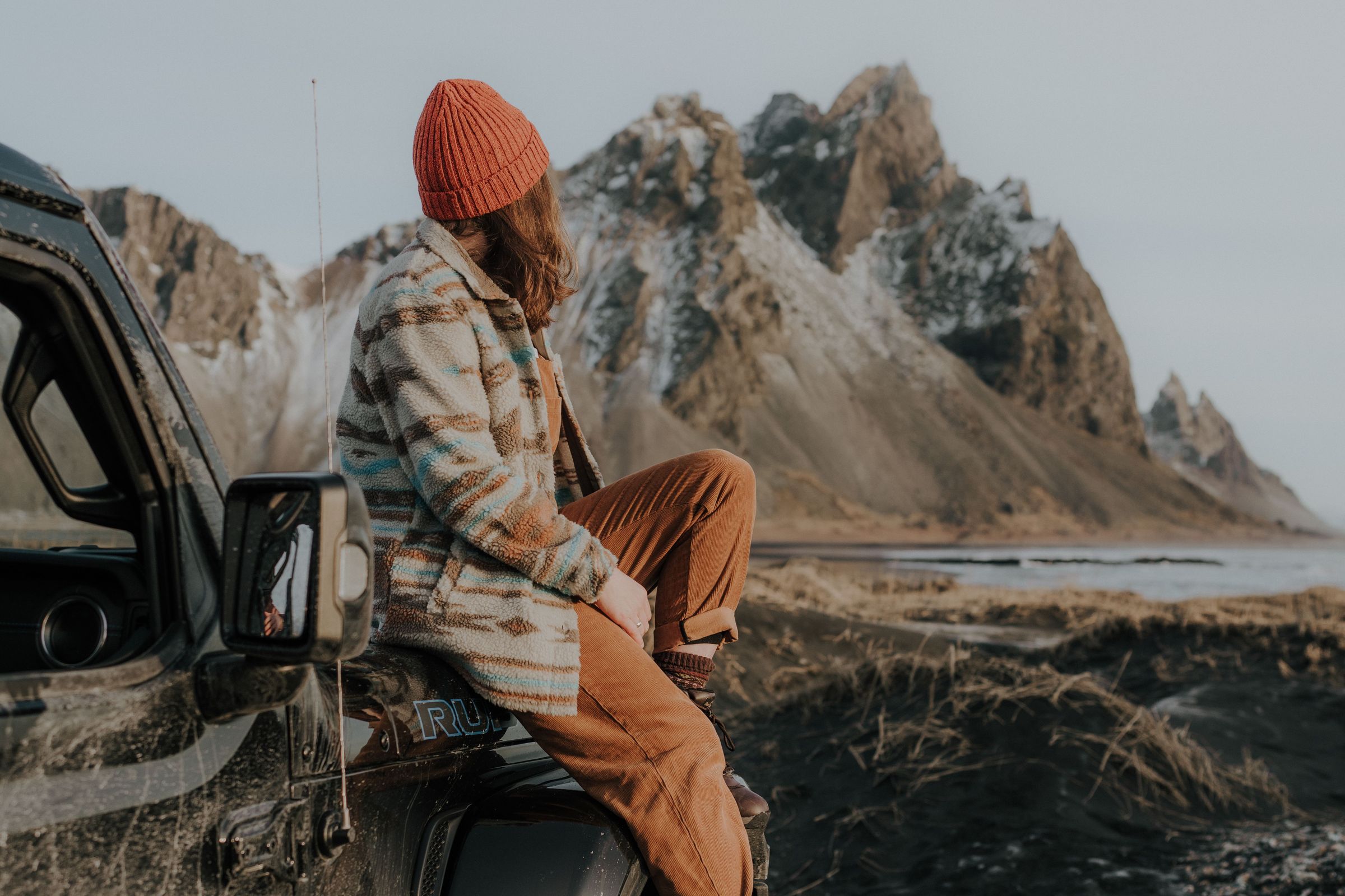 Girl sitting in the front of her car with mountains in the background