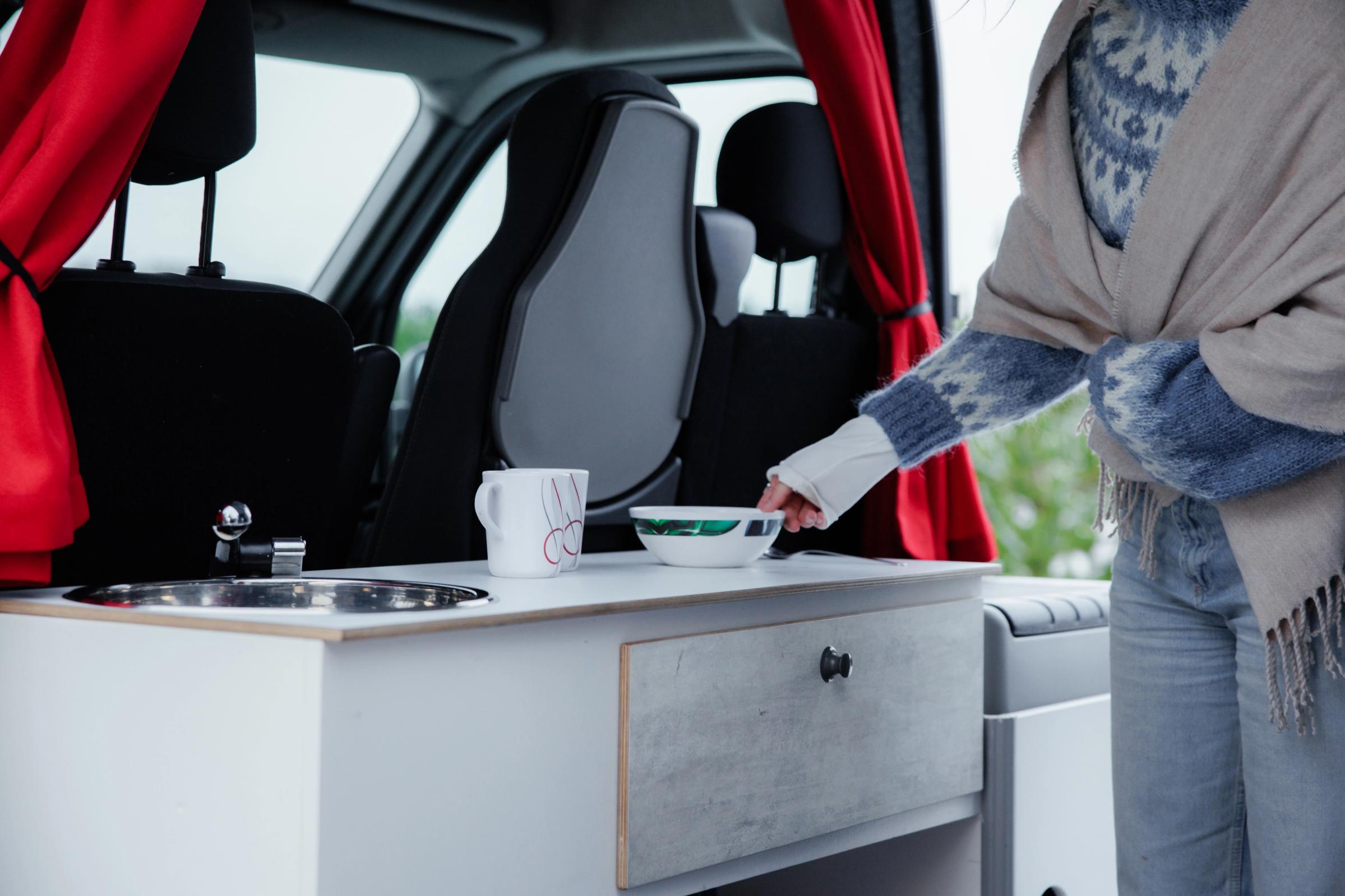 Eine Person stellt in einem großen Camper für fünf Personen eine Schüssel neben eine Tasse auf die Arbeitsfläche.