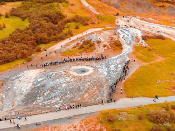 Aerial view of tourists around a geyser in a golden geothermal landscape.