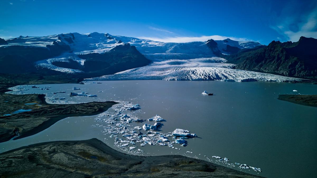 A glacial lagoon with icebergs, a glacier, mountains, and a small boat.